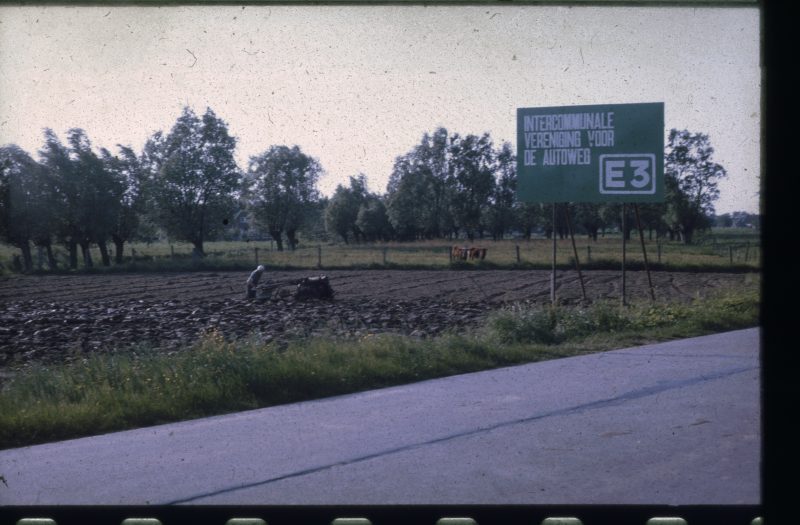 Bord waarop aanleg van de E3 werd aangekondigd, gelegen in een veld naast de oude weg in Deerlijk, tussen Vichte en Harelbeke. Wegens die aanleg verloor de boer op de foto, net als vele anderen, zijn grond.